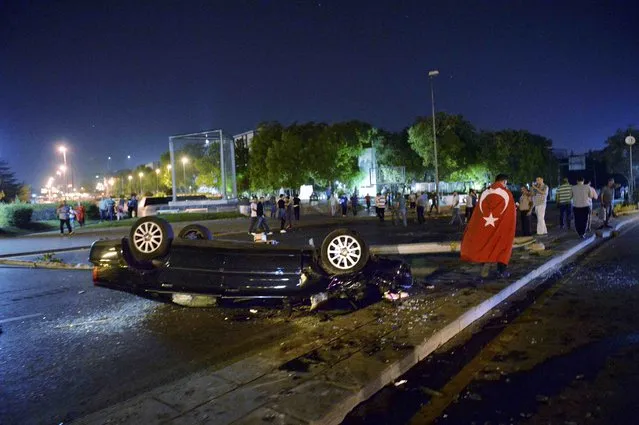 A man wearing a Turkish flag as a cape walks near a flipped car in Ankara, Turkey July 16, 2016. (Photo by Reuters/Stringer)