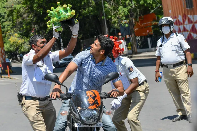 Traffic police personnel (L and R) wearing coronavirus-themed helmets perform in front of a motorist (C) as they participate in a campaign to educate the public during a government-imposed nationwide lockdown as a preventive measure against the COVID-19 coronavirus in Bangalore on March 31, 2020. (Photo by Manjunath Kiran/AFP Photo)