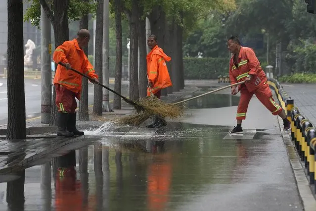 Workers clear a puddle of water after a rainstorm in Beijing, Sunday, August 14, 2022. (Photo by Ng Han Guan/AP Photo)