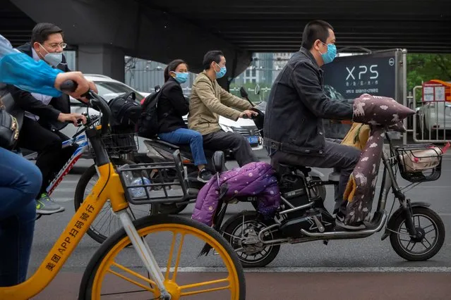 People pass by wearing face masks to protect against the spread of the new coronavirus as ride along a street in Beijing, Wednesday, May 6, 2020. China on Wednesday reported just two new cases of the coronavirus and no deaths. (Photo by Mark Schiefelbein/AP Photo)
