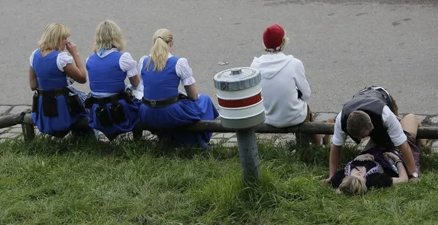 Waitresses rest besides visitors on a meadow on the opening day of the 181st Oktoberfest beer festival in Munich, southern Germany, Saturday, September 20, 2014. (Photo by Matthias Schrader/AP Photo)