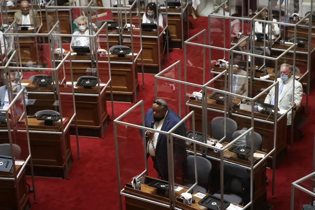 Rhode Island Democratic state Rep. Raymond Hull, below center, holds a microphone on the floor of the House Chamber while separated by plastic protective barriers at the start of a legislative session, Wednesday, June 17, 2020, at the Statehouse, in Providence, R.I. Wednesday's session was the first by the legislature to be held on the floor of the chamber since March of 2020 due to the coronavirus pandemic. (Photo by Steven Senne/AP Photo)