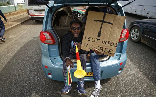 Protesters demanding President Robert Mugabe stand down ride in the back of a car with a placard “Rest in peace Mugabe” as they drive towards State House in Harare, Zimbabwe Saturday, November 18, 2017. In a euphoric gathering that just days ago would have drawn a police crackdown, crowds marched through Zimbabwe's capital on Saturday to demand the departure of President Robert Mugabe, one of Africa's last remaining liberation leaders, after nearly four decades in power. (Photo by Ben Curtis/AP Photo)