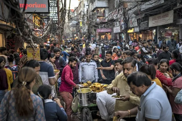 People eat street food as shoppers crowd a market in New Delhi, India, Saturday, November 12, 2022. The world's population is projected to hit an estimated 8 billion people on Tuesday, Nov. 15, according to a United Nations projection. (Photo by Altaf Qadri/AP Photo)