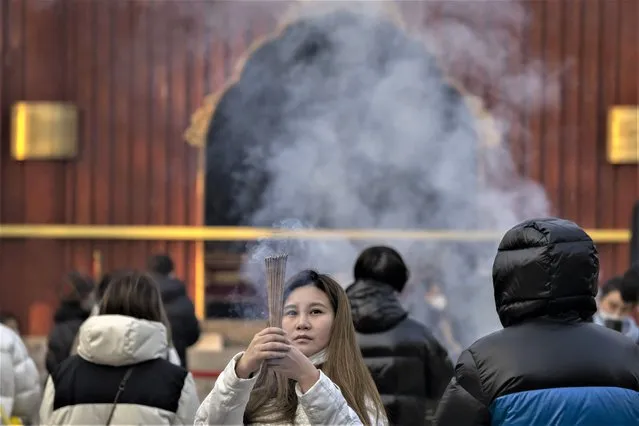 A visitor burns incense as she prays on the first day of the Lunar New Year holiday at the Lama Temple in Beijing, Sunday, January 22, 2023. (Photo by Mark Schiefelbein/AP Photo)