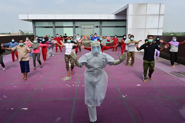 A gymnastics instructor wearing personal protective equipment (PPE) leads a morning exercise for patients of the COVID-19 coronavirus at a hotel designated to treat asymptomatic patients in Karawaci, Indonesia's Banten province on October 5, 2020. (Photo by Adek Berry/AFP Photo)