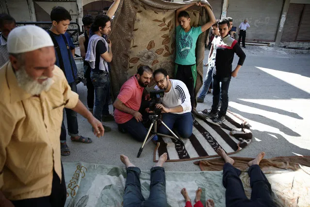 Syrian director Humam Husari (center left) and cameraman Sami al-Shami (center right) operate a camera as they film a scene in the rebel-held besieged town of Zamalka, in the Damascus suburbs, Syria September 19, 2016. (Photo by Bassam Khabieh/Reuters)