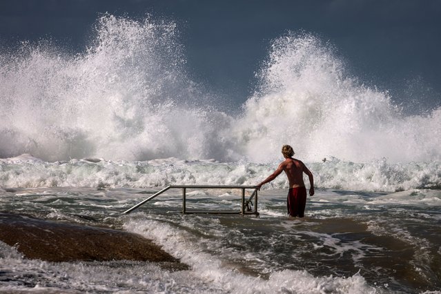 A man walks towards a wave breaking on a rock pool at North Narrabeen Beach in Sydney on April 18, 2025, as large swells hit the east coast of Australia. (Photo by David Gray/AFP Photo)