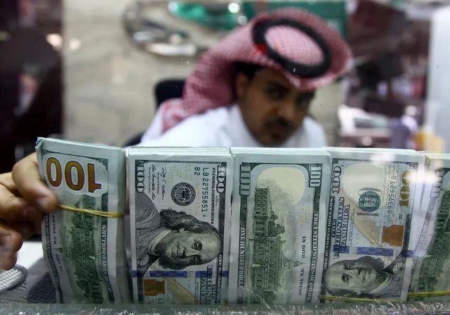 A Saudi money changer, pictured through a glass, arranges U.S banknotes at a currency exchange shop in Riyadh, Saudi Arabia September 29, 2016. (Photo by Faisal Al Nasser/Reuters)