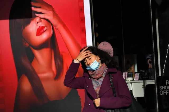 A Romanian young woman wearing a mask arranges her hair while passing a lipstick advertise in downtown Bucharest, Romania, 21 October 2020. Due to rising numbers of coronavirus infections, authorities have implemented the “red scenario” for Buchrest since two days. School courses will take place exclusively online and kindergartens were closed in Bucharest, while wearing a mask became mandatory in all public spaces, starting from 20 October. It is now forbidden to go in cinemas, closed performance venues, gambling halls and casinos. Restaurants can serve customers only on their outdoor terraces, and hotels will serve only accommodated guests inside their restaurants. (Photo by Robert Ghement/EPA/EFE)