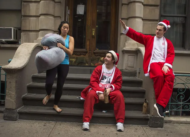 Revelers dressed in holiday theme costumes drink alcohol as a woman comes out with her laundry during SantaCon in New York Saturday, December 12, 2015, in New York. As thousands of Santa-suited merrymakers prepare to hit the city's streets and bars, organizers of the annual pub crawl say they're taking more steps than ever to deter naughty behavior. (Photo by Andres Kudacki/AP Photo)