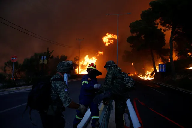 Firefighters and soldiers fall back as a wildfire burns in the town of Rafina, near Athens, Greece, July 23, 2018. (Photo by Costas Baltas/Reuters)