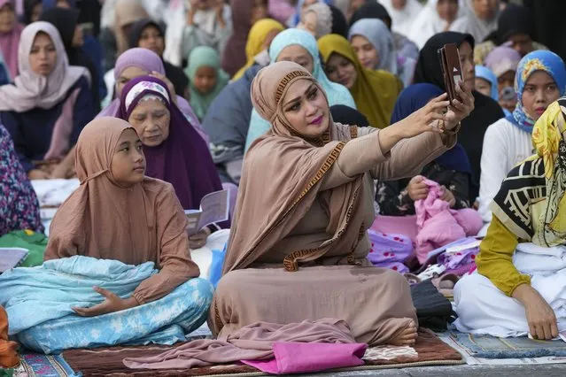 A woman takes a selfie before a morning prayer marking the Eid al-Adha holiday on a street in Jakarta, Indonesia, Thursday, June 29, 2023. Muslims around the world will celebrate Eid al-Adha, or the Feast of the Sacrifice, slaughtering sheep, goats, cows and camels to commemorate Prophet Abraham's readiness to sacrifice his son Ismail on God's command. (Photo by Tatan Syuflana/AP Photo)