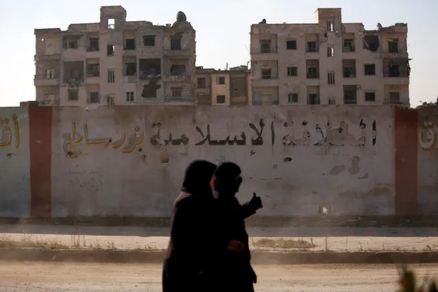 Women walk near damaged buildings in government controlled Hanono housing district in Aleppo, Syria December 4, 2016. The calligraphy on the wall reads “The Islamic Caliphate is Shining light”. (Photo by Omar Sanadiki/Reuters)