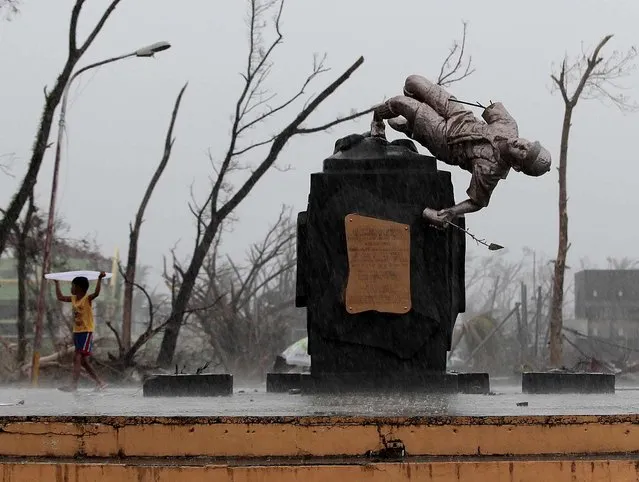 A survivor uses a plastic cover to protect him from rain as he passes by a damaged Boy Scout statue in typhoon ravaged Tacloban, Philippines, on November 12, 2013. Typhoon Haiyan, one of the strongest storms on record, slammed into six central Philippine islands on Friday. (Photo by Aaron Favila/Associated Press)