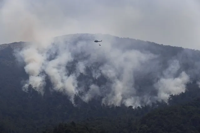 A Lebanese army helicopter flies over a forest fire on an extinguishing mission, at Qobayat village, in the northern Akkar province, Lebanon, Thursday, July 29, 2021. (Photo by Hussein Malla/AP Photo)