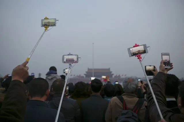 People use selfie sticks and lift up their mobile phones and cameras to record and take pictures of a flag-raising ceremony at Tiananmen Square as the area near the Great Hall of the People is prepared for upcoming annual sessions of the National People's Congress (NPC) and Chinese People's Political Consultative Conference (CPPCC) in Beijing March 3, 2016. (Photo by Damir Sagolj/Reuters)