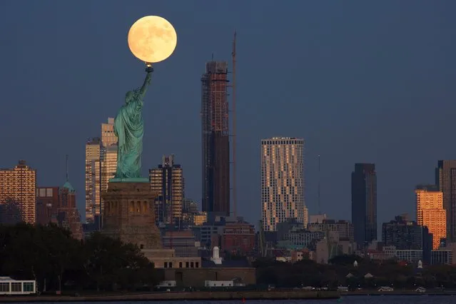 The Hunter's Moon rises at a size of 99.6 percent behind Statue of Liberty and 9 DeKalb Avenue on the skyline of Brooklyn as the sun sets in New York City on October 19, 2021 as seen from Jersey City, New Jersey. (Photo by Gary Hershorn/Getty Images)