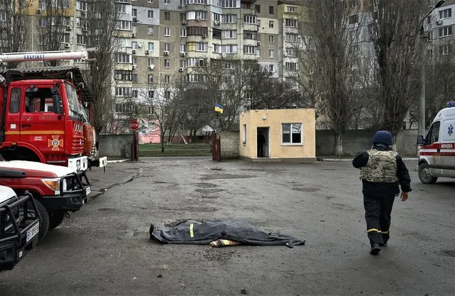 A firefighter passes by the dead body of a firefighter killed in the Russian shelling of the fire station in Kherson, Ukraine, on the Orthodox Christmas Eve Friday, January 6, 2023. (Photo by LIBKOS/AP Photo)