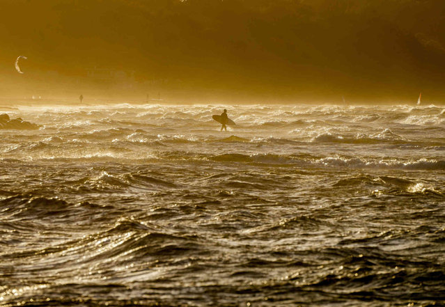 A surfer walks in the breakers of the Baltic Sea near Weissenhaeuser Strand, northern Germany, on a stormy Friday, October 22, 2021. (Photo by Michael Probst/AP Photo)