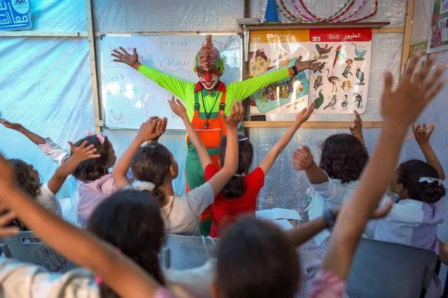 A man dressed as a clown entertains children at a makeshift school in a camp for displaced Palestinians in Deir El-Balah, in the central Gaza strip on April 27, 2024, amid the ongoing conflict between Israel and the militant Hamas group. (Photo by AFP Photo/Stringer)