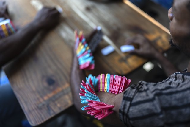 Clothespins pinch the arm of a domino player, each pin symbolizing when he loses, at a public school that serves as a shelter for people displaced from their homes due to clashes between armed gangs, in Port-au-Prince, Haiti, April 22, 2024. (Photo by Ramon Espinosa/AP Photo)