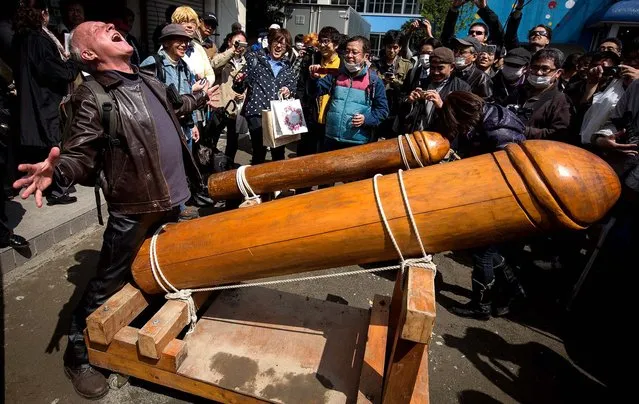 A man poses for photographers with a large wooden phallic sculpture during Kanamara Matsuri (Festival of the Steel Phallus) in Kawasaki, Japan, on April 6, 2014. The festival has become a popular tourist attraction and is used to raise money for HIV awareness and research.  (Photo by Chris McGrath/Getty Images)
