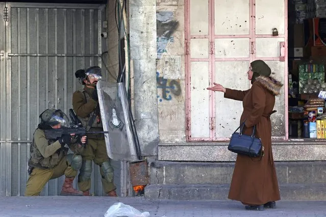 A woman gestures at Israeli security forces firing rubber-bullets to disperse Palestinian stone-throwers amid clashes in the West Bank town of Hebron, on February 9, 2022. Israeli forces killed three Palestinians on February 8 during a daytime raid against what Israel described as a “terrorist cell”, leaving a vehicle in the West Bank city of Nablus riddled with bullet holes. (Photo by Hazem Bader/AFP Photo)