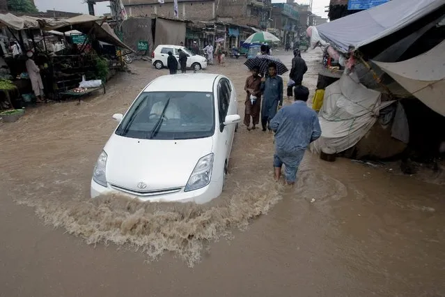 A car drives through a flooded street after heavy rains in a suburb of Peshawar, Pakistan, Thursday, July 23, 2015. (Photo by Mohammad Sajjad/AP Photo)