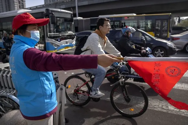 A crossing guard wearing a face mask directs a bicyclist at an intersection in Beijing, Tuesday, April 12, 2022. The U.S. has ordered all non-emergency consular staff to leave Shanghai, which is under a tight lockdown to contain a COVID-19 surge. (Photo by Mark Schiefelbein/AP Photo)