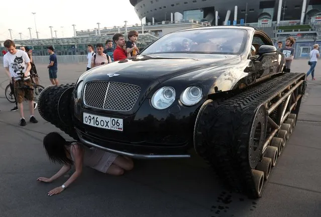 A woman poses for a picture next to a caterpillar-tracked Bentley Continental GT, which was modified by Russian car engineering enthusiasts, during a demonstration in St. Petersburg, Russia on June 7, 2019. (Photo by Anton Vaganov/Reuters)