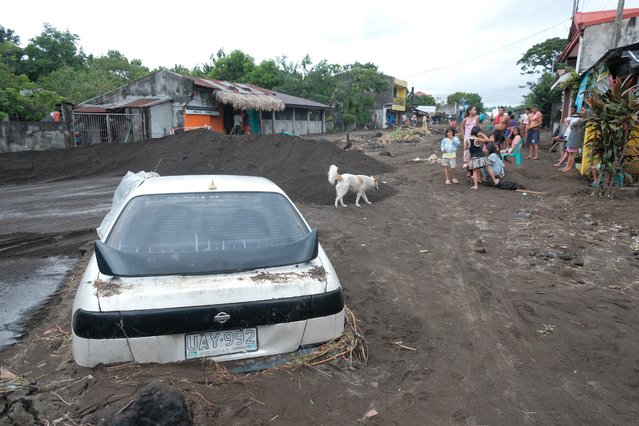 Residents stay beside a car partially buried by volcanic mud that had flowed down from Mayon volcano after heavy rains caused by Tropical Storm Trami hit Guinobatan town, Albay province, Philippines on Wednesday October 23, 2024. (Photo by John Michael Magdasoc/AP Photo)