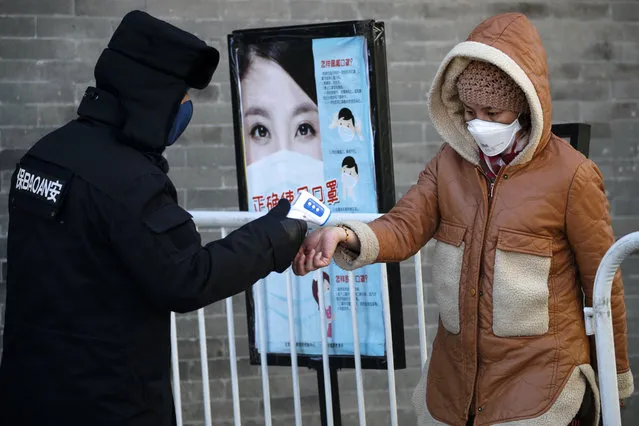 A woman wearing a protective face mask receives a temperature check from a security guard as she enters Qianmen Street, a popular tourist spot, in Beijing, Sunday, February 16, 2020. China reported Sunday a drop in new virus cases for the third straight day, as it became apparent that the country's leadership was aware of the potential gravity of the situation well before the alarm was sounded. (Photo by Andy Wong/AP Photo)