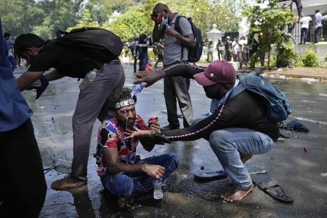 A protester helps another after police fired teargas to disperse them before they stormed Sri Lankan Prime Minister Ranil Wickremesinghe's office, demanding he resign after president Gotabaya Rajapaksa fled the country amid economic crisis in Colombo, Sri Lanka, Wednesday, July 13, 2022. (Photo by Eranga Jayawardena/AP Photo)