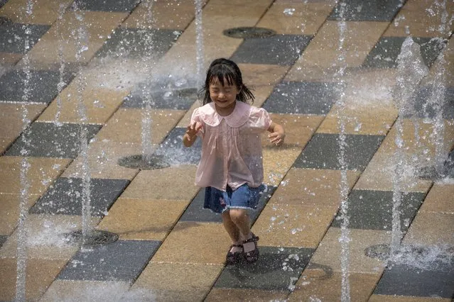 A girl runs through a fountain at an outdoor shopping area on an unseasonably hot day in Beijing, Saturday, June 25, 2022. From the snowcapped peaks of Tibet to the tropical island of Hainan, China is sweltering under the worst heatwave in decades while rainfall hit records in June. (Photo by Mark Schiefelbein/AP Photo)