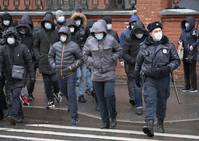 A policeman, foreground right, accompanies a group of migrant laborers, who came to renew work permits, to a migration center in St.Petersburg, Russia, Thursday, April 2, 2020. President Vladimir Putin on Thursday ordered most Russians to stay off work until the end of the month as part of a partial industrial shutdown to curb the spread of the coronavirus. (Photo by Dmitri Lovetsky/AP Photo)
