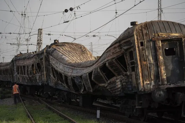 A railway worker stands next to heavily damaged train after a Russian attack on a train station during Ukraine's Independence Day in the village of Chaplyne, Ukraine, Thursday, August 25, 2022. (Photo by Leo Correa/AP Photo)