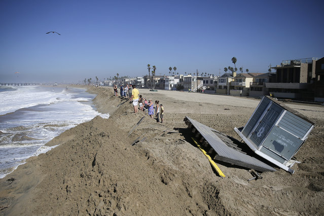 A lifeguard tower knocked over by high tides sits on the beach as people stand on the sand wall on Wednesday, Aug. 27, 2014, in Seal Beach, Calif. Parts of the low-lying Southern California coastal community of Seal Beach has been inundated by a surge of rising seawater brought on by Hurricane Marie spinning off Mexico's Pacific coast. (AP Photo/Jae C. Hong)