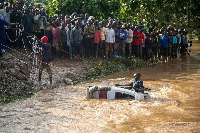 Villagers try to retreive the bodies of 14 people from a minibus in the river Nabuyonga at Namakwekwe, eastern Uganda, on August 1, 2022. The number of people killed in flash floods in the eastern Ugandan city of Mbale has jumped to 22, including a group of partygoers who became trapped in a minibus, police said on Monday. Two rivers burst their banks at the weekend after the city was battered by heavy rainfall, leading to mudslides that inflicted widespread damage and left many residents homeless. (Photo by Badru Katumba/AFP Photo)