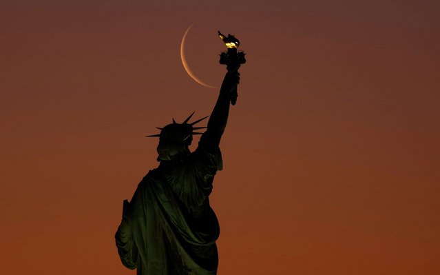 A waning crescent moon is seen behind the Statue of Liberty in New York on Thursday, March 27, 2025. (Photo by Gary Hershorn/Corbis News/Getty Images)
