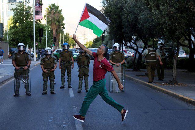 A demonstrator holds up a Palestinian flag in front of riot police officers during a rally in support of Palestinian people in Gaza in front of Israeli embassy, amid the ongoing conflict between Israel and Hamas, in Santiago, Chile on March 4, 2024. (Photo by Ivan Alvarado/Reuters)