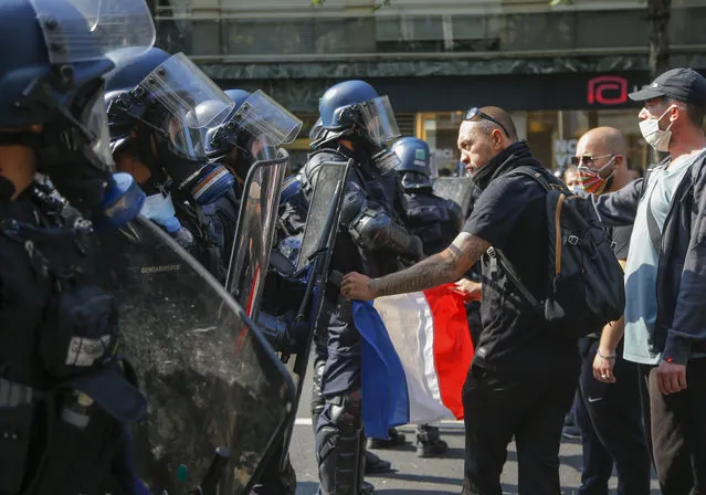 A yellow vest protester holds a French flag as he faces French riot police during a march in Paris, Saturday, September 12, 2020. Activists relaunched France's yellow vest movement Saturday after the disruptive demonstrations against Emmanuel Macron's presidency and perceived elitism tapered off during the coronavirus pandemic. (Photo by Michel Euler/AP Photo)