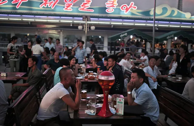 North Koreans enjoy beer and snacks during Taedonggang Beer Festival in Pyongyang, North Korea, Sunday, August 21, 2016. The festival, the first of its kind in the country, was held as a promotional event for the locally brewed beer. Korean signs in the background read “Our country is the best”. (Photo by Dita Alangkara/AP Photo)