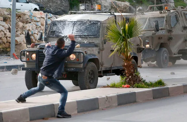Palestinians throw stones at Israeli army vehicles after forces entered the village of Halhoul in the occupied West Bank on February 07, 2018. A Palestinian stabbed a security guard at the entrance to an Israeli settlement and was shot dead in the latest violence in the occupied West Bank, Israel' s military said. (Photo by Hazem Bader/AFP Photo)