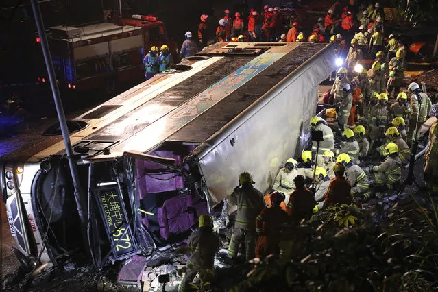 Firemen hurry to try to remove injured passengers from a double-decker lying on its side in Hong Kong, Saturday, February 10, 2018. A double-decker bus crashed in a Hong Kong suburb on Saturday evening, killing 18 people and injuring dozens more, authorities in the southern Chinese city said. (Photo by Apple Daily via AP Photo)