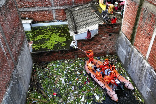 Members of India's National Disaster Response Force distribute food supplies to stranded residents in a submerged area following heavy monsoon rains along the banks of the River Ganga, in Prayagraj, India, August 5, 2025. (Photo by Rajesh Kumar Singh/AP Photo)