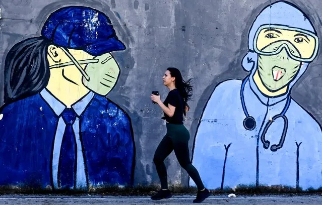 A woman runs in front of a mural  inspired by the COVID-19 coronavirus pandemic in in Skopje, North Macedonia, 30 October 2020. The number of newly infected COVID-19 patients over 24 hourse in North Macedonia rose to a record number since the pandemic began.The capacity of the hospitals in the country are very close to be full. The Macedonian parliament voted on changes in the legislation regarding the protection of the public from infectious diseases. These changes make wearing face masks mandatory outside of the home. (Photo by Georgi Licovski/EPA/EFE)