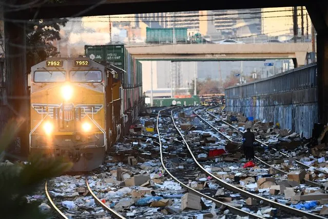 A person carries items collected from the train tracks as a Union Pacific locomotive passes through a section of Union Pacific train tracks littered with thousands of opened boxes and packages stolen from cargo shipping containers, targeted by thieves as the trains stop in downtown Los Angeles, California on January 14, 2022. (Photo by Patrick T. Fallon/AFP Photo)