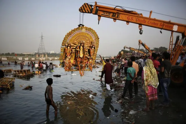 A giant Idol of Hindu goddess Durga suspends from a crane before it is immersed in the River Yamuna during Durga Puja festival in New Delhi, India, Tuesday, October 11, 2016. The immersion of idols marks the end of the festival that commemorates the slaying of a demon king by lion-riding, 10-armed goddess Durga, marking the triumph of good over evil. (Photo by Altaf Qadri/AP Photo)