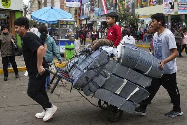 Stuart Rodriguez gets a ride on a dolly of jean fabric bought at the Gamarra textile market as his brothers Steve and Stevenson transport the load to their father's factory in Lima, Peru, Thursday, August 8, 2024. (Photo by Guadalupe Pardo/AP Photo)